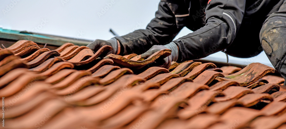 Dachdecker nimmt bei der Sanierung einen alten Tonziegel aus der Deckung